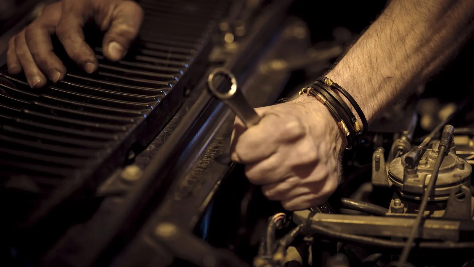 A mechanic's hands working on a car engine with a spanner