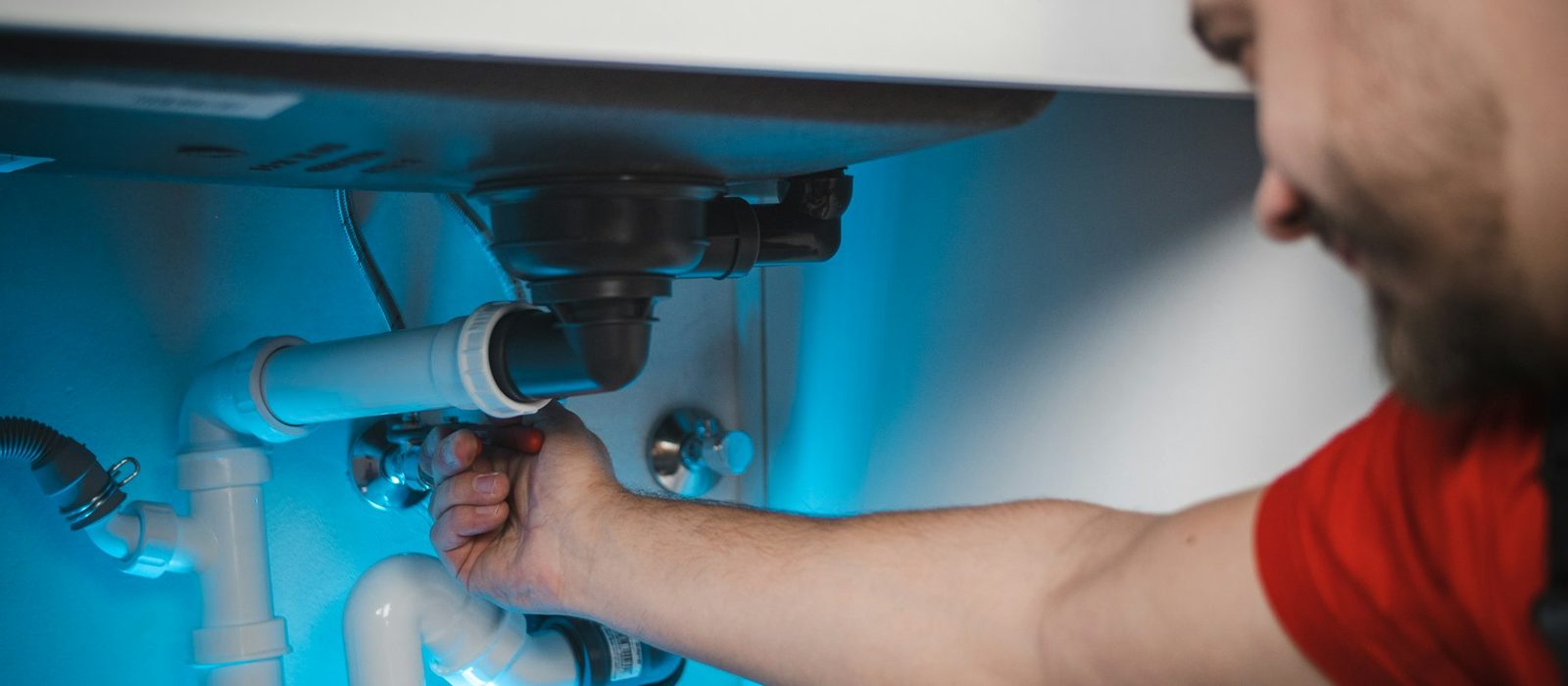 A plumber tightening a waste pipe under a sink