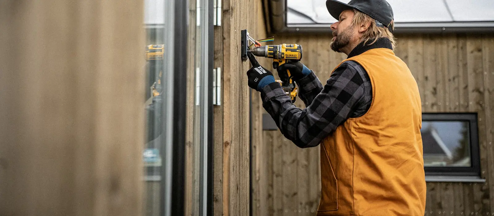 A tradesman fitting an outdoor electrical box to a timber wall with a cordless drill